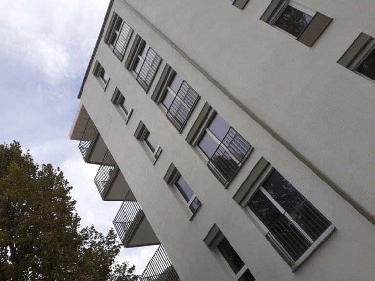 Perspektivischer Blick an der Fassade eines Wohngebäudes mit Balkonen und Fensterläden.