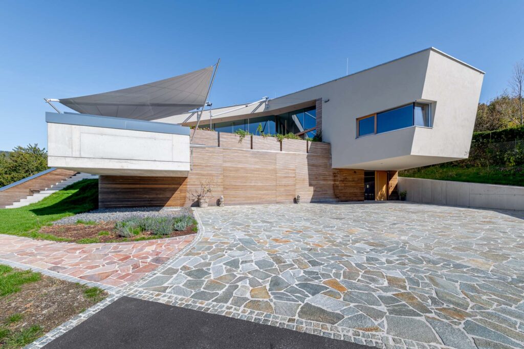 Die markante Zufahrt mit Natursteinbelag und Vorsprüngen im Beton setzt architektonische Akzente.