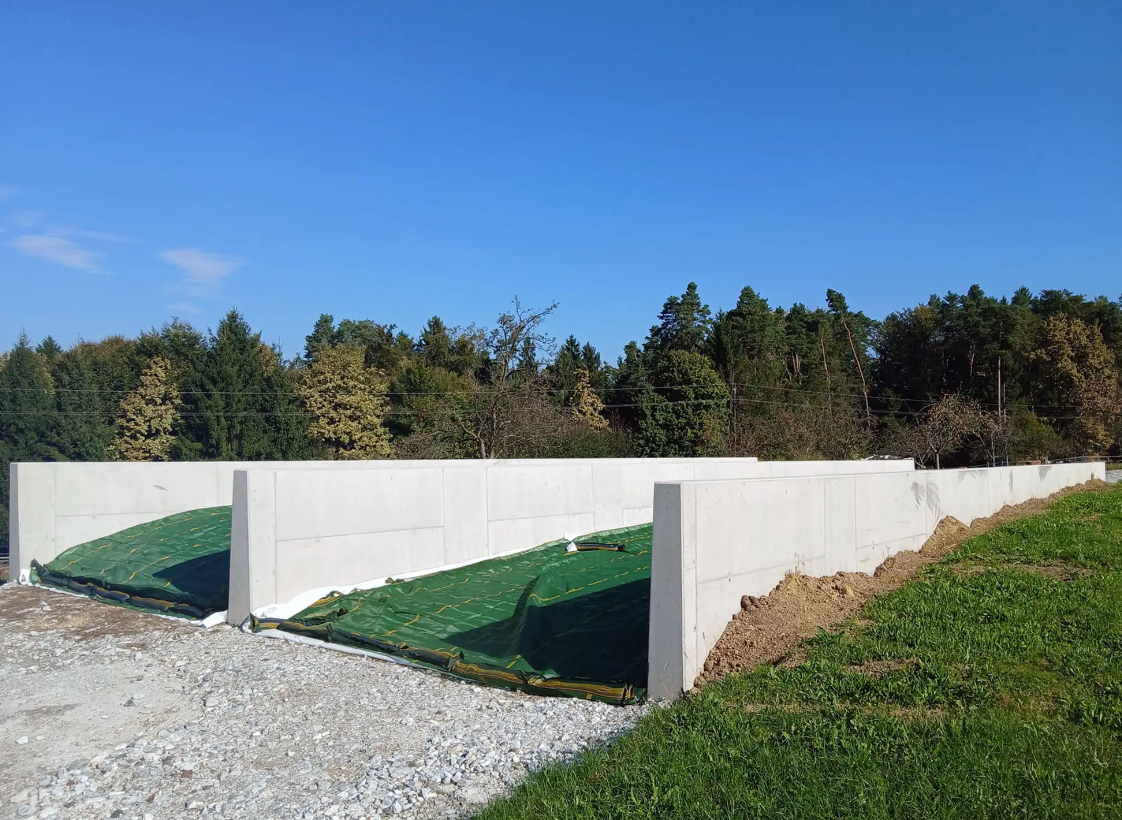 Offenes landwirtschaftliches Silolager aus Betonwänden mit abgedecktem Erntegut auf einer Wiese in der Steiermark