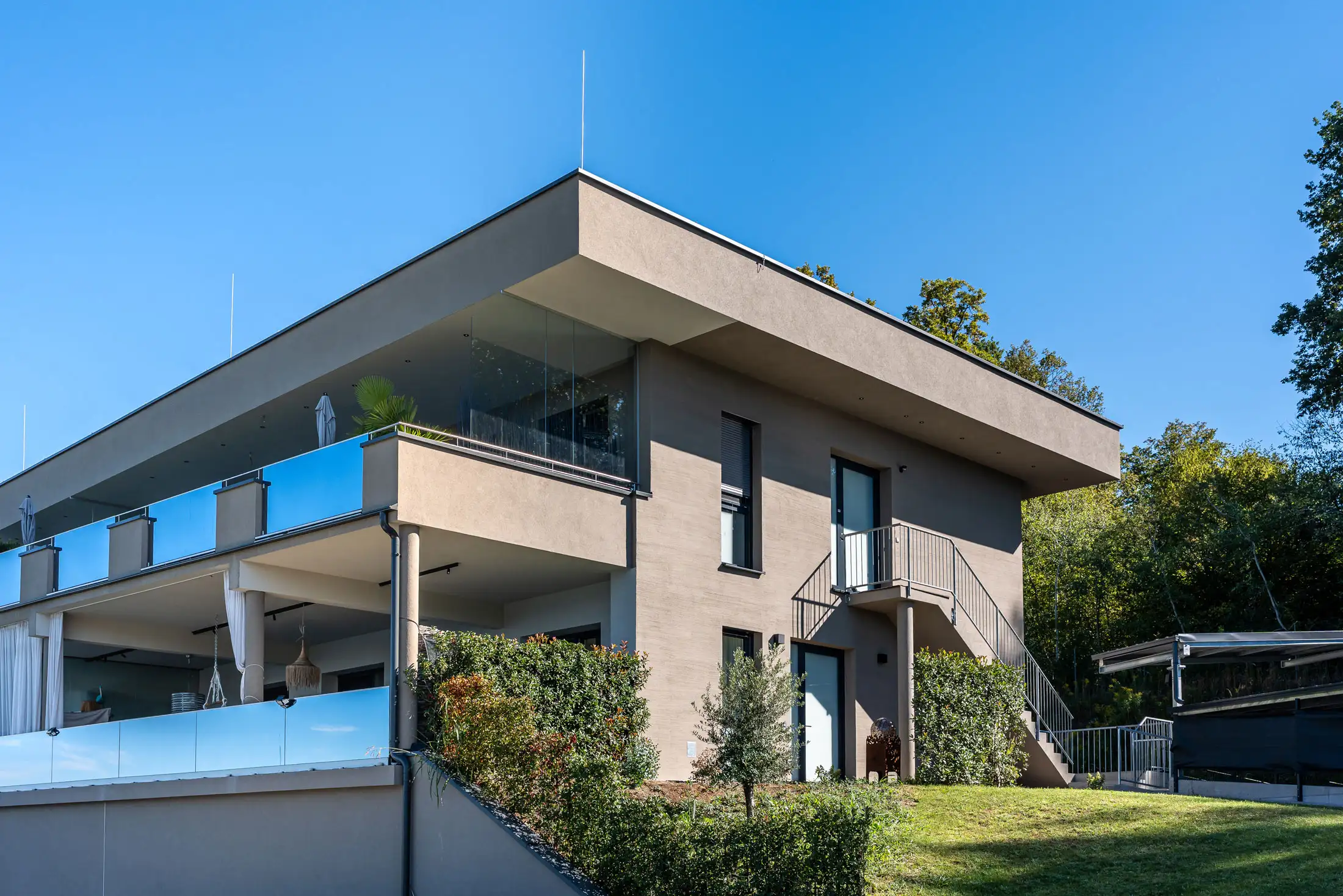 Modernes Wohnhaus mit frischer Fassadengestaltung, großzügigen Terrassen und Glasbrüstungen in Hanglage in der Steiermark Moderne Fassadengestaltung eines Gastronomiebetriebs mit großen Terrassenflächen und Glasbrüstungen in Hanglage in der Steiermark