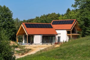 Einfamilienhaus in Hanglage mit heller Fassade, zwei versetzten roten Ziegeldächern und Photovoltaikmodulen auf beiden Dachflächen.