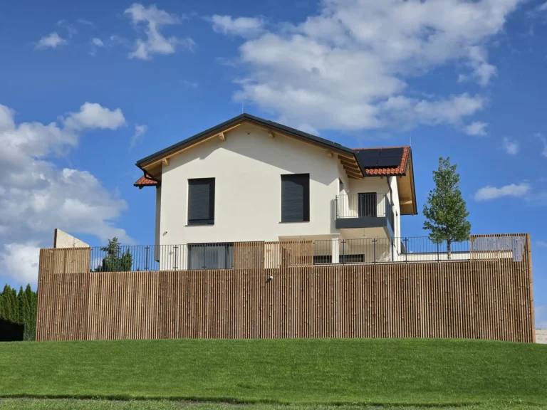 Einfamilienhaus in Trofaiach hinter einer breiten Rasenfläche mit Holzlamellen vor der Terrasse und seitlichem Balkon.