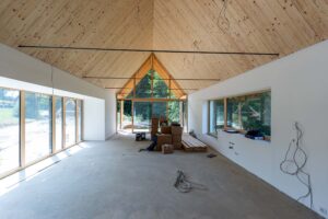 Großer Innenraum im Ausbau mit sichtbarer Holzdecke bis zum First, breiten Fensterflächen und verglaster Giebelseite.
