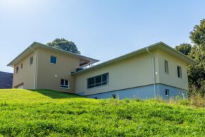 Hausansicht mit abgeschrägtem Gelände und Waldrand im Hintergrund Titel: Wohnhaus in leichter Hanglage mit Panoramablick