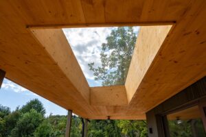 Rechteckige Öffnung in einer Terrassenüberdachung aus Holz mit Blick auf den Himmel und eine Baumkrone.