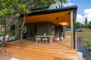 Überdachte Holzterrasse mit breiten Stufen, Esstisch und Sitzbereich vor einer dunklen Holzfassade.